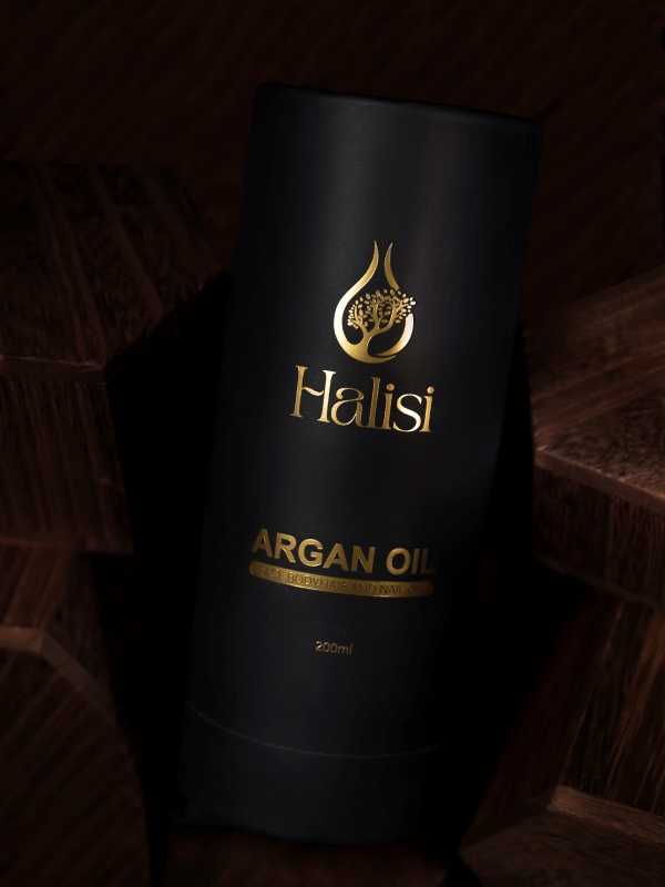 Elegant Black And Gold Halisi Argan Oil Product Packaging Displayed On Dark Wooden Blocks.